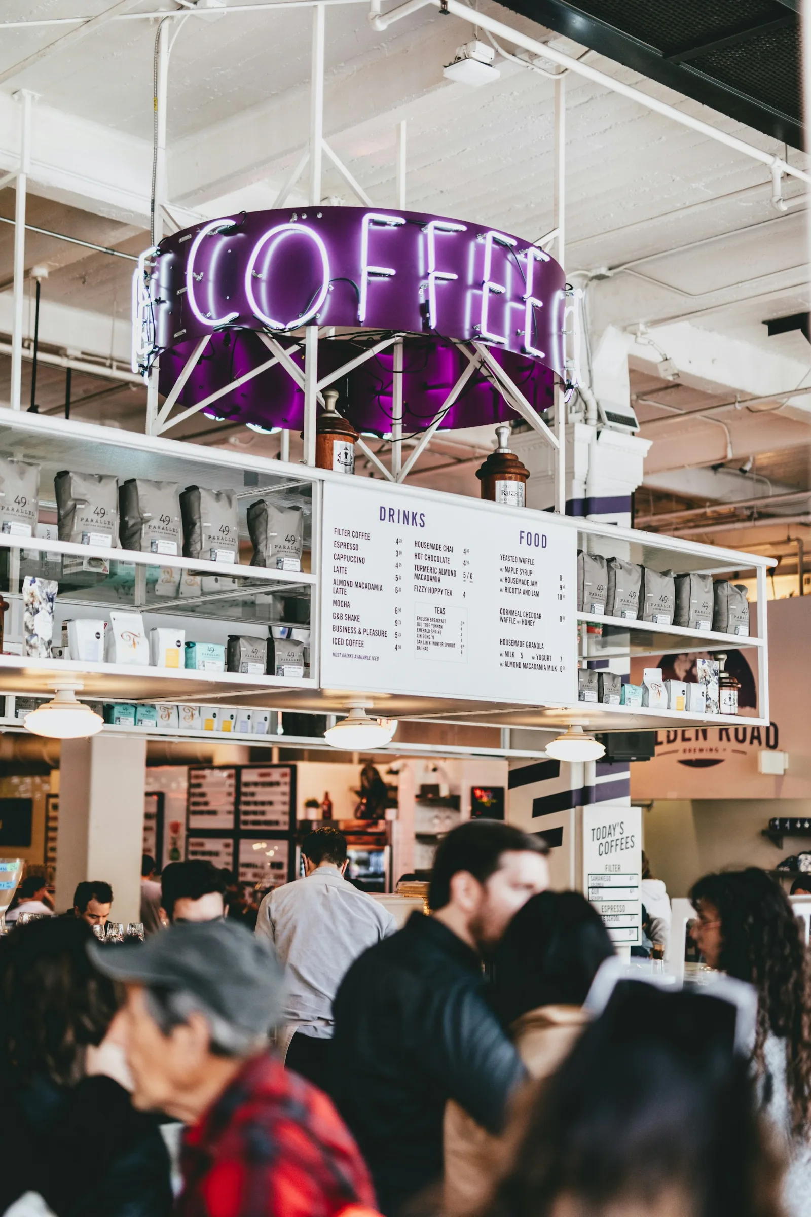A busy coffee bar with people gathered beneath a neon coffee sign