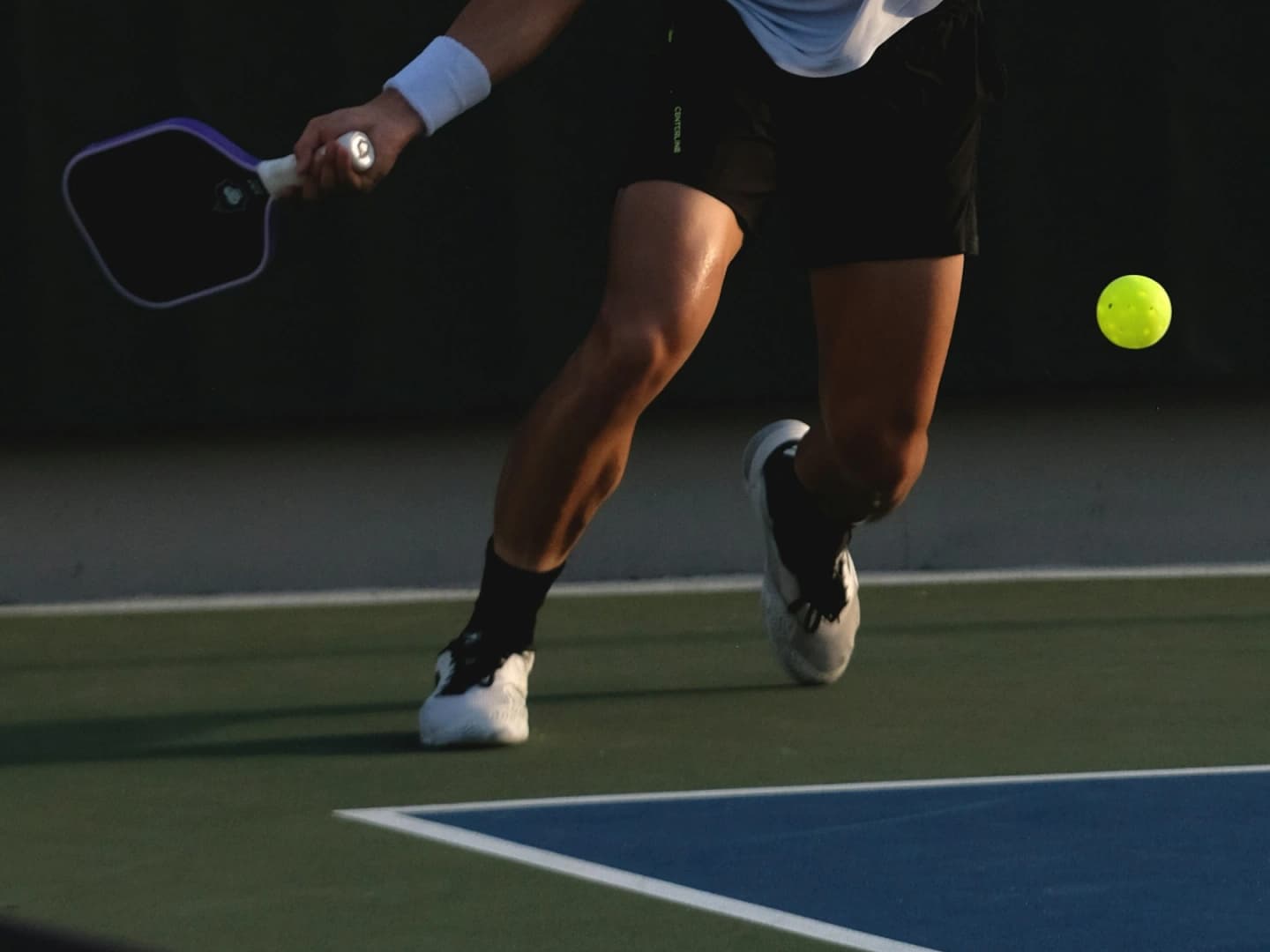 A pickleball player reaching for a low ball during a match