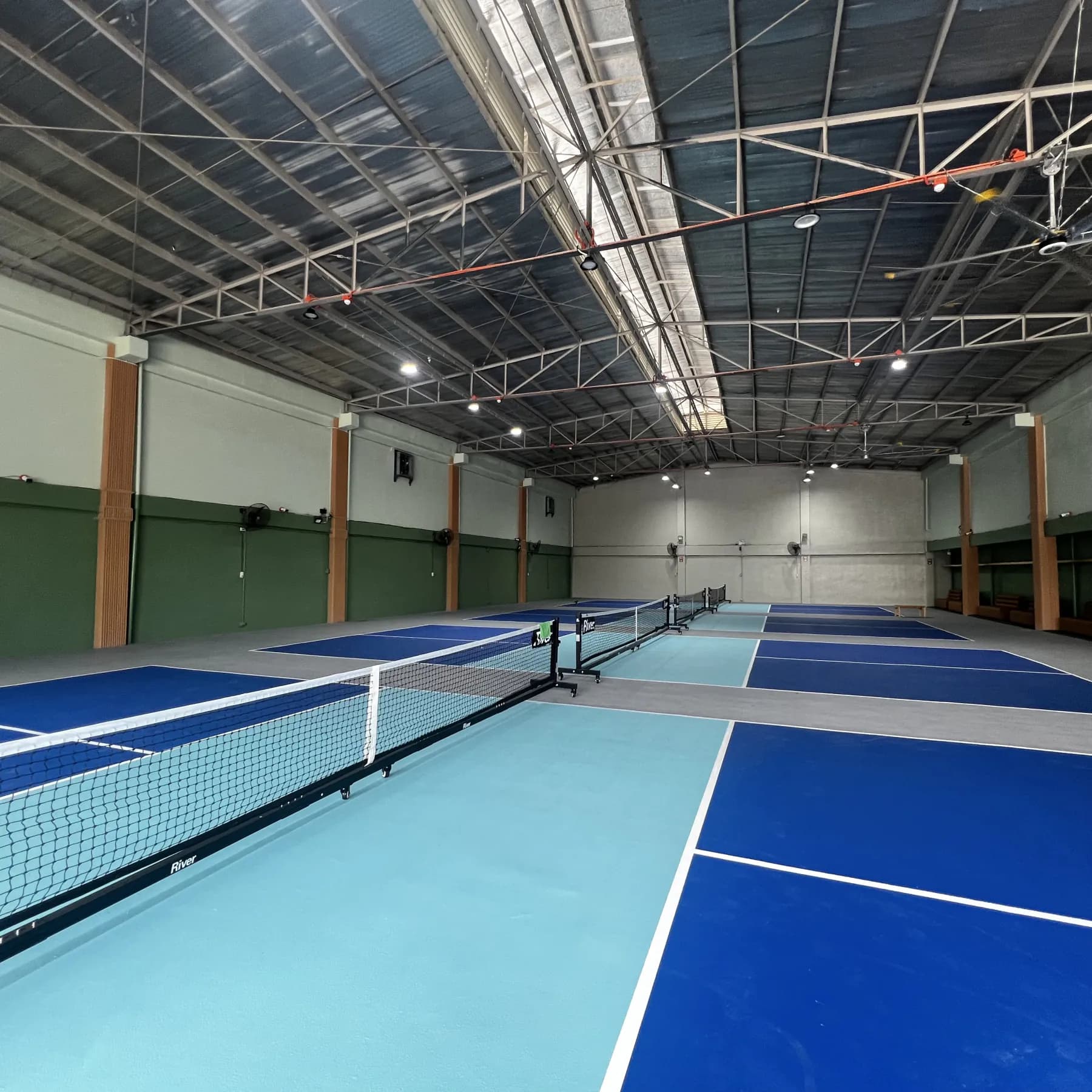 A row of indoor blue pickleball courts beneath a steel roof